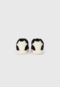 Baskets en suède noir avec des accents crème, présentant un talon arrondi et une semelle en caoutchouc. Design minimaliste avec une texture lisse. Lignes simples et épurées.