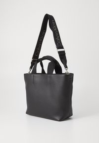 Borsa a spalla in pelle nera con doppi manici superiori e tracolla rimovibile, con il logo "Calvin Klein". Texture liscia e design minimalista.