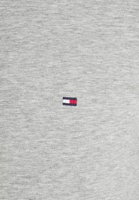 Graues Baumwoll-T-Shirt mit einem kleinen gestickten Logo und roten, weißen und blauen Streifen. Glatte Textur, Rundhalsausschnitt.