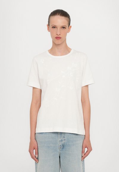T-shirt en coton blanc avec un col rond, des manches courtes et une broderie florale subtile en fil ton sur ton sur le devant.