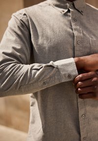 Grijze langetermijnshirt gemaakt van stevige stof met een knoopsluiting aan de voorkant, kraag en knoopmanchetten. Bevat een detail van een borstzak.