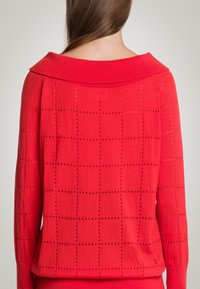 Czerwony sweter dzianinowy z szerokim kołnierzem, o luźnym splocie i kwadratowych wzorach, z długimi rękawami. Miękka tekstura z luźnym krojem.