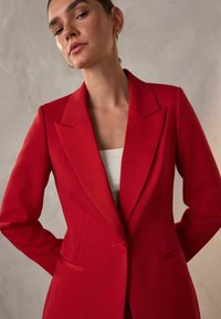 Rød skræddersyet blazer med skarpe klapper, enkelt knappelukning og forlommer. Glat stof med en struktureret pasform, elegant snit.