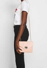 Borsa a tracolla in finta pelle rosa con chiusura in tono oro, dotata di patta pieghevole e tracolla a catena. Texture liscia e forma rettangolare.