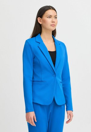 Světle modrý blejzr z hladké tkaniny s jedním knoflíkem, s klopami a bočními kapsami. Model jej má na sobě přes černý top.