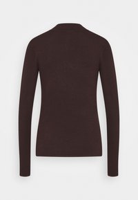 Tummanruskea pitkähihaisen istuva neule näkyy takaa vaalealla taustalla.