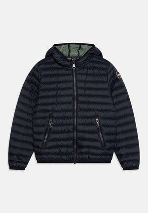 Veste matelassée à capuche bleu marine avec fermeture éclair à l’avant, poches latérales zippées, poignets élastiques et écusson rond avec logo sur la manche gauche.