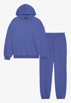 Paarse sweatshirt met capuchon en lange mouwen, gecombineerd met bijpassende joggerbroek. Beide items hebben een zachte textuur en elastische boorden.