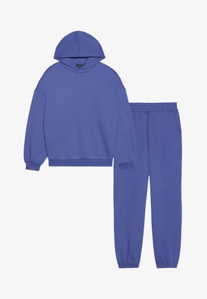 Pulover violet cu glugă și mâneci lungi, purtat cu pantaloni jogger asortați. Ambele articole prezintă o textură moale și manșete elastice.