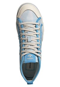 Siniset kangasketjut, joissa on valkoisia kumikoristeita, tasaiset nauhat ja logopaneeli. Rakenne on teksturoitu, pyöreä kärki ja vahvistetut nauhapaikat.