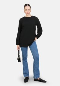 Haut noir à manches longues avec un col rond ; associé à un jean évasé bleu clair. Accentué par un petit sac à main noir et des chaussures noires à enfiler.