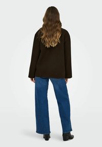 Su�éter oversized marrón oscuro con mangas largas, combinado con jeans de pierna ancha azul y botas de tacón negras, mostrado desde la parte posterior.