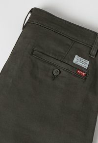 Σκούρο πράσινο παντελόνι Levi's με πίσω τσεπάκι με κουμπί και ορατές κόκκινες και λευκές ετικέτες Levi's.