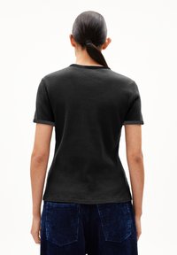 T-shirt noir à côtes avec des manches courtes et un col rond, associé à un pantalon en velours côtelé bleu foncé avec des poches arrière.