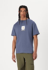 Tricou din bumbac albastru cu mâneci scurte, având un grafic pătrat cu un soare și textul "Quiksilver" pe piept. Design simplu, croială lejeră.