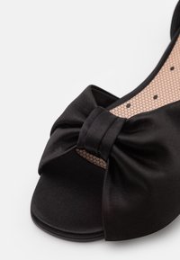 Scarpa open-toe in satin nero con un prominente dettaglio a fiocco sul davanti. La soletta presenta un motivo testurizzato con piccoli esagoni.