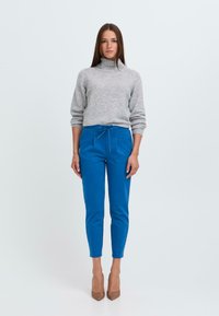 Grau Rollkragenpullover, weiche Textur, kombiniert mit leuchtend blauen tapered Hosen mit Kordelzugbund und zwei Fronttaschen. Braune Absätze.