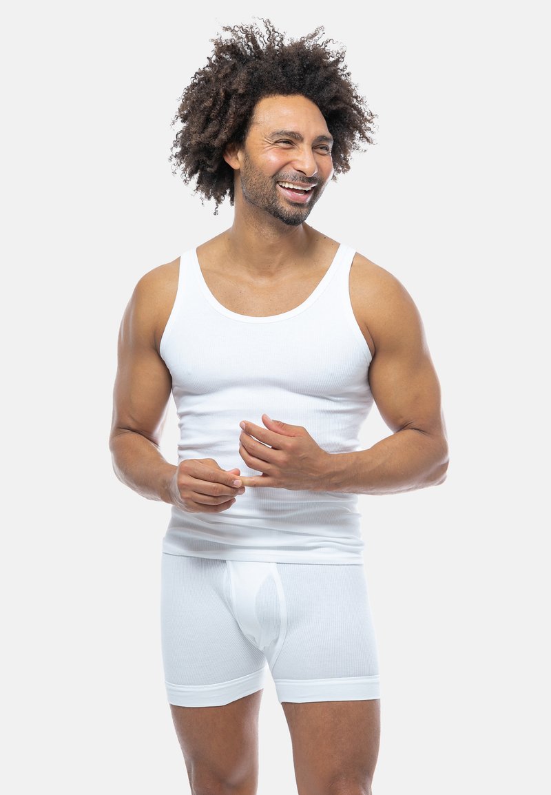 Canotta bianca in cotone e boxer, texture a coste, che presenta una vestibilità aderente. Il modello sta in posa in modo casual, con le mani leggermente alzate.