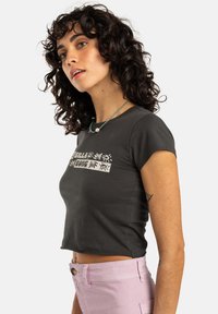 Grå cropped t-skjorte med korte ermer, med hvit grafisk tekst og blomsterdesign. Kombinert med lyserosa høytlivsbukser.