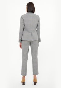 Traje de cuadros gris con un blazer a medida y pantalones de corte slim. Presenta detalles en azul y naranja, botones decorativos y una abertura en la parte trasera.