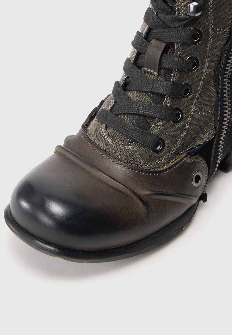 Zbliżenie na brązowo-czarny skórzany but z płótna, z czarnymi sznurówkami i zamkiem błyskawicznym na białym tle.