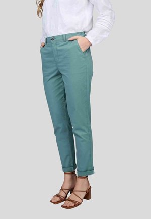 Pantalon en coton bleu-vert à coupe slim, avec des poignets retroussés et des poches avant, associé à des sandales à talons blocs marron avec des lanières.