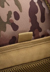 Tarnmusterstoff in Braun-, Grün- und Beigetönen; mit beigem Netz und Nähten; umfasst ein kleines Stoffschlaufen-Detail.