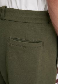 Pantalons tricotés vert olive avec une texture lisse, dotés d'une poche arrière et d'une taille à onglets. Design minimaliste sans quincaillerie visible.