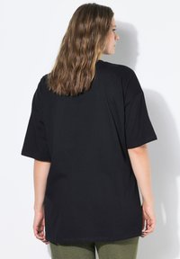 Camiseta negra de gran tamaño con mangas cortas, hecha de un tejido suave y ligero. Diseño liso con un corte relajado, sin patrones ni acentos visibles.