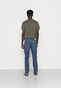 Dark green cotton t-shirt, relaxed fit, paired with blue denim jeans. Jeans feature a straight leg, five pockets, and minimal stitching.