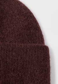 Burgundy knitted beanie made from soft wool, featuring a textured, fuzzy finish and a folded cuff at the bottom.
