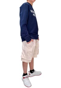 Felpa navy con scritte bianche, pantaloni cargo beige e sneakers bianche con accenti rossi. Outfit comodo e casual per il clima caldo.