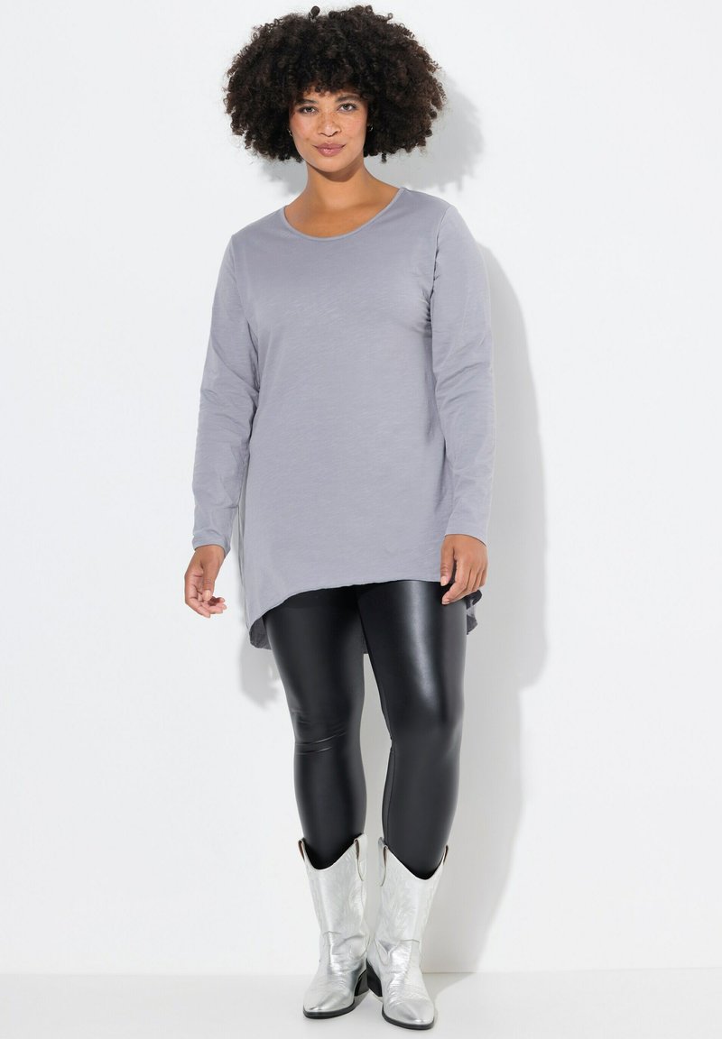 Hellgraues Langarm-Tunikakleid mit rundem Ausschnitt, kombiniert mit schwarzen Leggings und metallisch silbernen Cowboy-Stiefeln. Glatte Textur, leicht abgerundeter Saum.