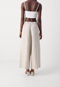 Beige široké kalhoty s elastickým pasem a zadní kapsou, kombinované s bílým crop topem a chunky podpatkovými sandály.