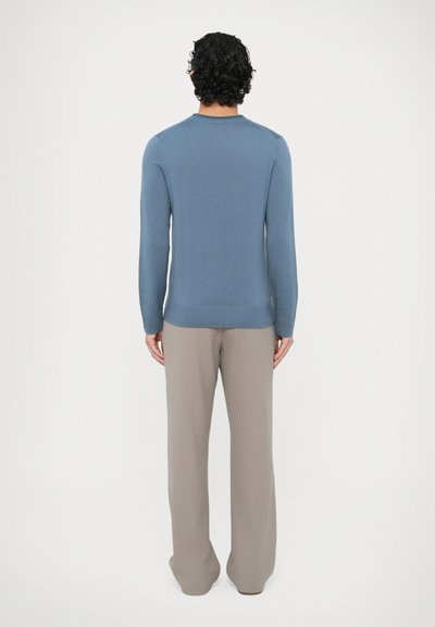 Niebieski dziany sweter z długimi rękawami i prążkowanym wykończeniem, zestawiony z szerokimi, jasnoszarymi spodniami. Faktura wydaje się miękka i lekko dopasowana.