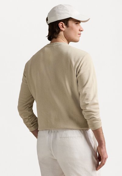 Beige színű, hosszú ujjú póló, kerek nyakkivágással, bordázott mandzsettákkal és strukturált felülettel, világos színű, lazán illeszkedő nadrággal párosítva.