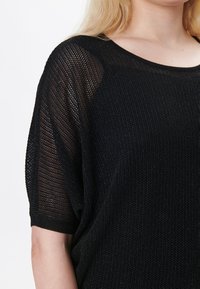 Maglione nero lavorato a maglia con una vestibilità ampia, maniche raglan corte e un motivo a tessitura aperta texture. Materiale morbido e leggero.