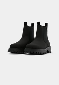 Sorte Chelsea-støvler laget av glatt materiale, med en kraftig såle og elastiske sidepaneler med pull-tabs for enkel påkledning.