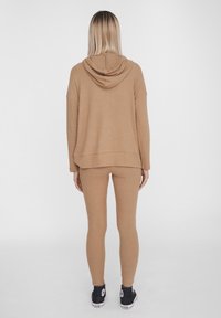 Felpa a costine di colore marrone chiaro con una vestibilità ampia e cappuccio sul retro, abbinata a leggings marrone chiaro aderenti. Completa con sneakers nere.