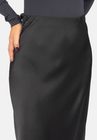 Schwarzer Satinrock mit einer glatten Textur und einer taillierten Silhouette. Der Bund ist gerafft und verleiht dem Design eine subtile Note.