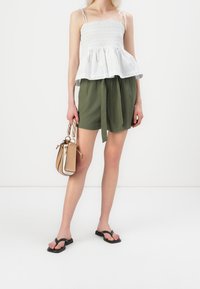 Haut blanc rayé avec smocks et ourlet évasé, assorti à un short vert à cordon de serrage ; tenant un petit sac à main beige ; tongs noires.