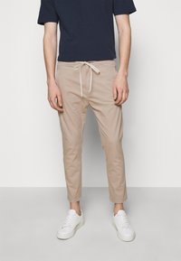 Beige chinos with a drawstring waist, featuring a slim fit and smooth cotton fabric, paired with white sneakers and a navy t-shirt.