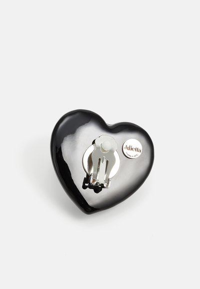 Pince à cheveux noire en forme de cœur, fabriquée en plastique brillant, avec un clip métallique et un accent logo argenté. Texture lisse avec une surface brillante.