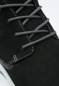 Černé semišové boty s šedými tkaničkami. Vyznačují se bílým prošíváním kolem okraje a zaobleným designem špičky pro elegantní vzhled.