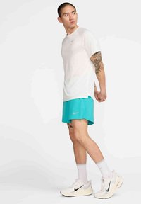 Vaaleanharmaa urheilupaita lyhyillä hihoilla, yhdistetty turkooseihin shortseihin ja valkoisiin juoksukenkihin. Varustettu Nike-logolla vaatteissa.