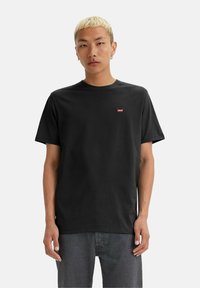 Sort bomulds t-shirt med korte ærmer, rund halsudskæring og lille rød Levi's-logo på brystet; parret med grå denimjeans.