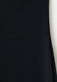 Tissu noir avec un détail de couture horizontale au milieu, montrant la texture et les coutures d’un vêtement sur un fond clair.