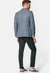 Dwurzędowa marynarka w niebiesko-białą kratkę o sztywnym kroju, w zestawieniu z ciemnozielonymi spodniami i szarymi trampkami. Casulowy i nowoczesny wygląd.