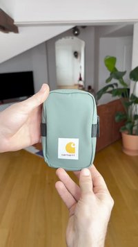 Mint zelena torbica iz mehkega materiala z belo Carhartt logotipom in črnim zadrgo. Velikost, ki udobno ustreza dlani.