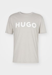 Béžové tričko s krátkým rukávem a kulatým výstřihem, na přední straně s velkým bílým nápisem "HUGO".